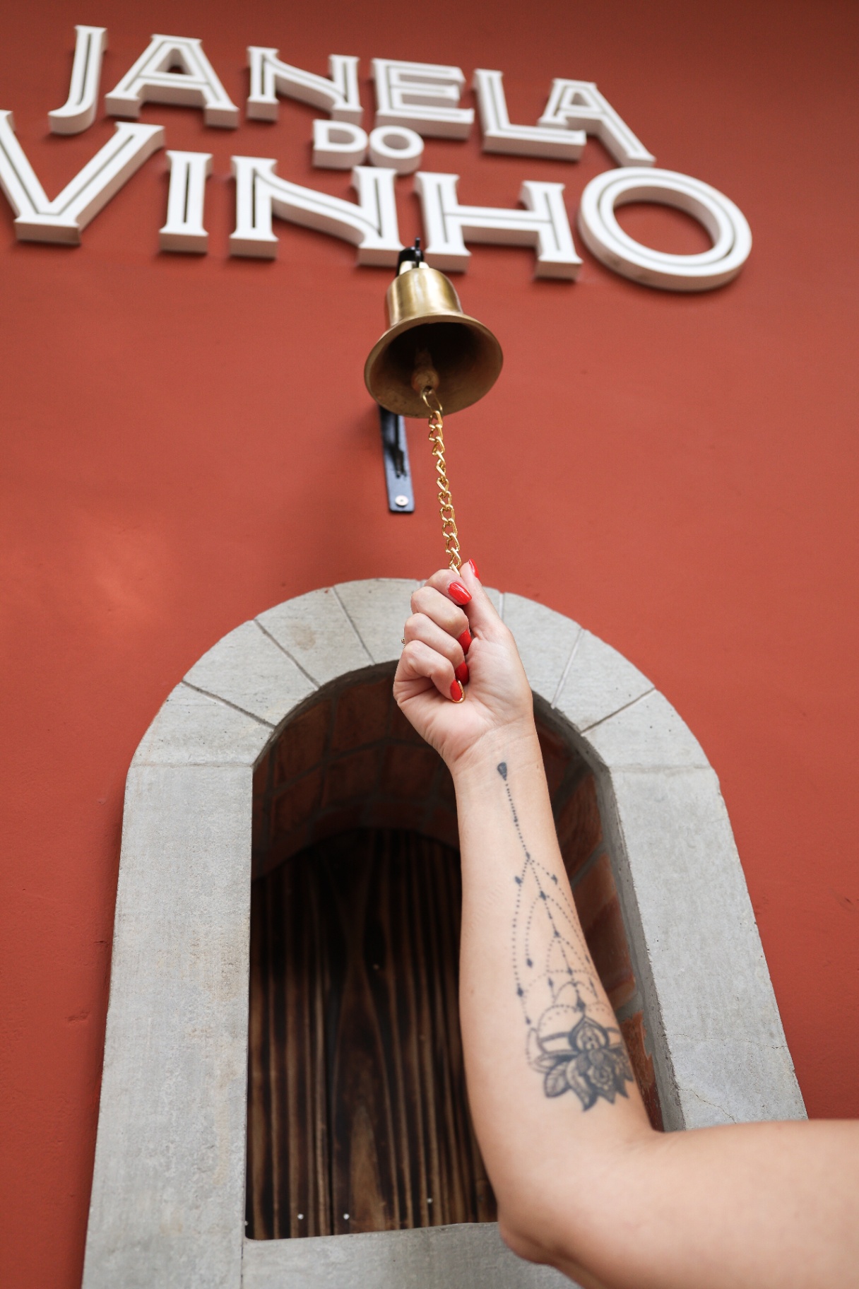 Mão tocando o sino de bronze acima da buchetta da Janela do Vinho